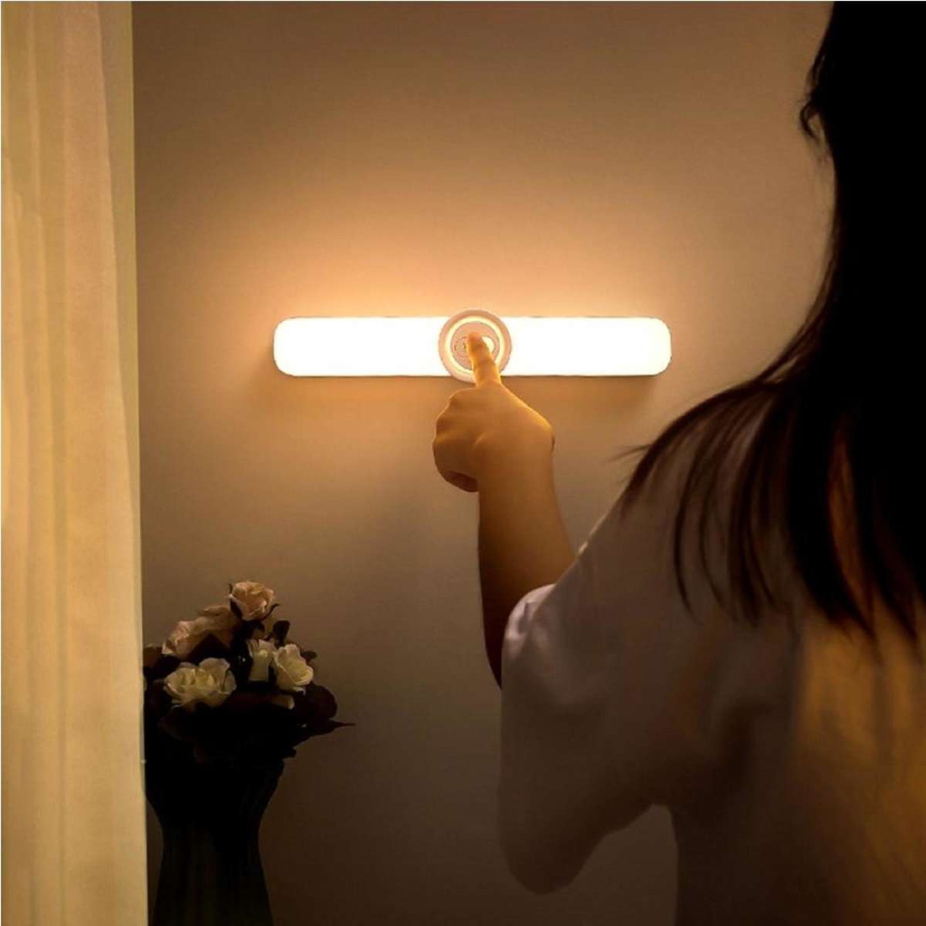 Person adjusting a wall-mounted light fixture with a warm glow.