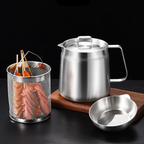 Stainless steel teapot, mesh basket with sticks, and small dish on a dark surface.
