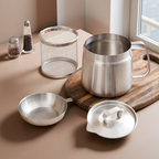 Set of stainless steel kitchenware including a pot, bowl, and lid on a wooden cutting board.