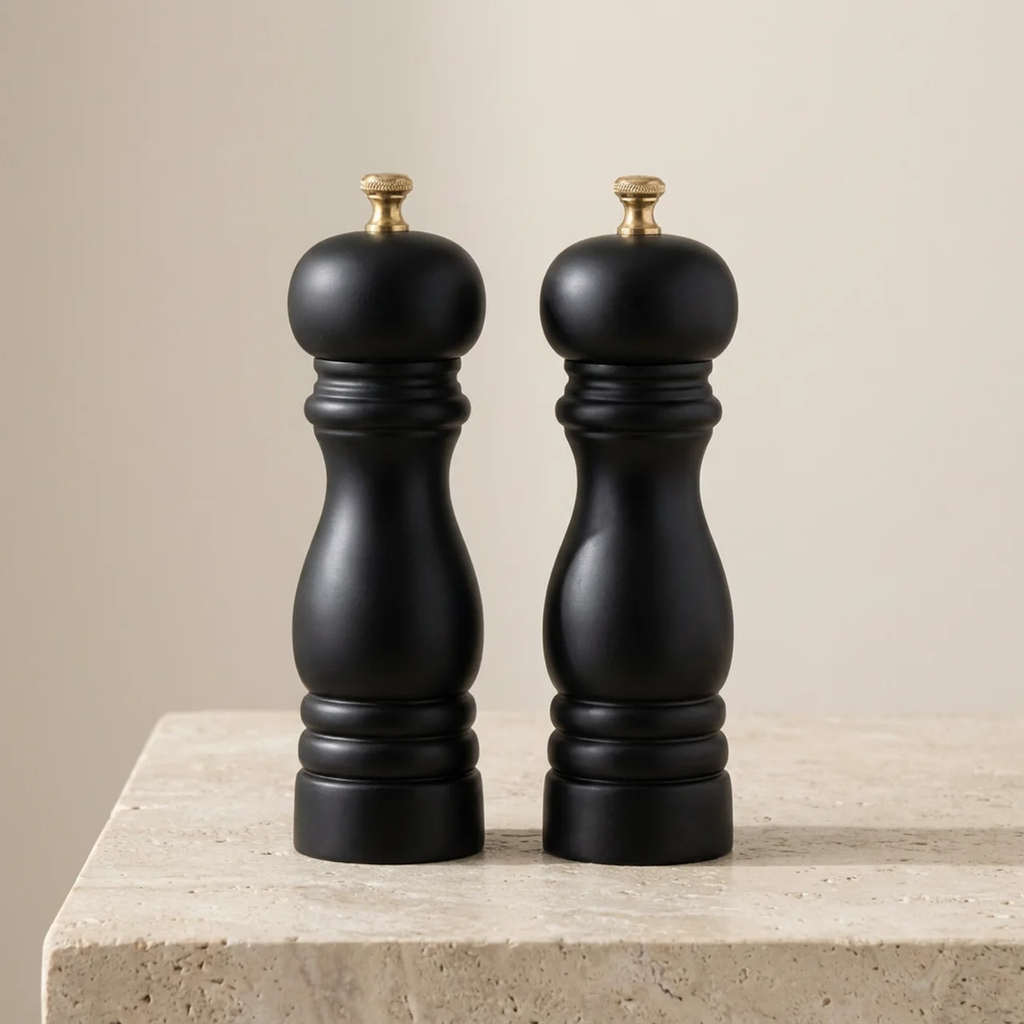 Two black pepper mills on a beige surface with a neutral background