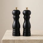 Two black pepper mills on a beige surface with a neutral background