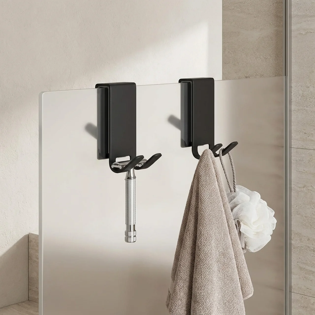 Black wall hooks with a towel and decorative item on a tiled wall.