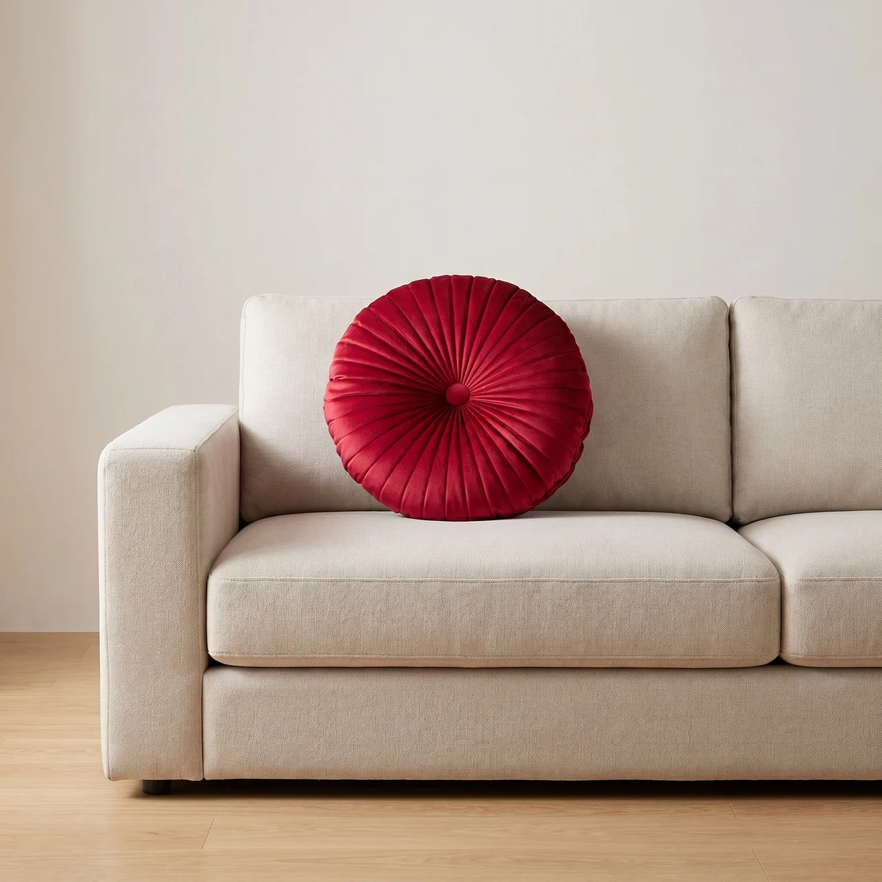 Beige sofa with a red round pillow against a plain wall