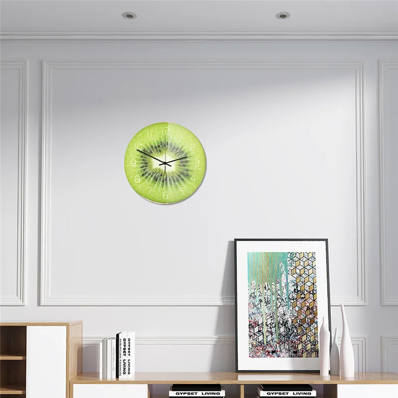 Green kiwi wall clock on a white wall with a framed picture below.