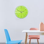 Green wall clock on a light gray wall above a white table with pink and blue chairs.