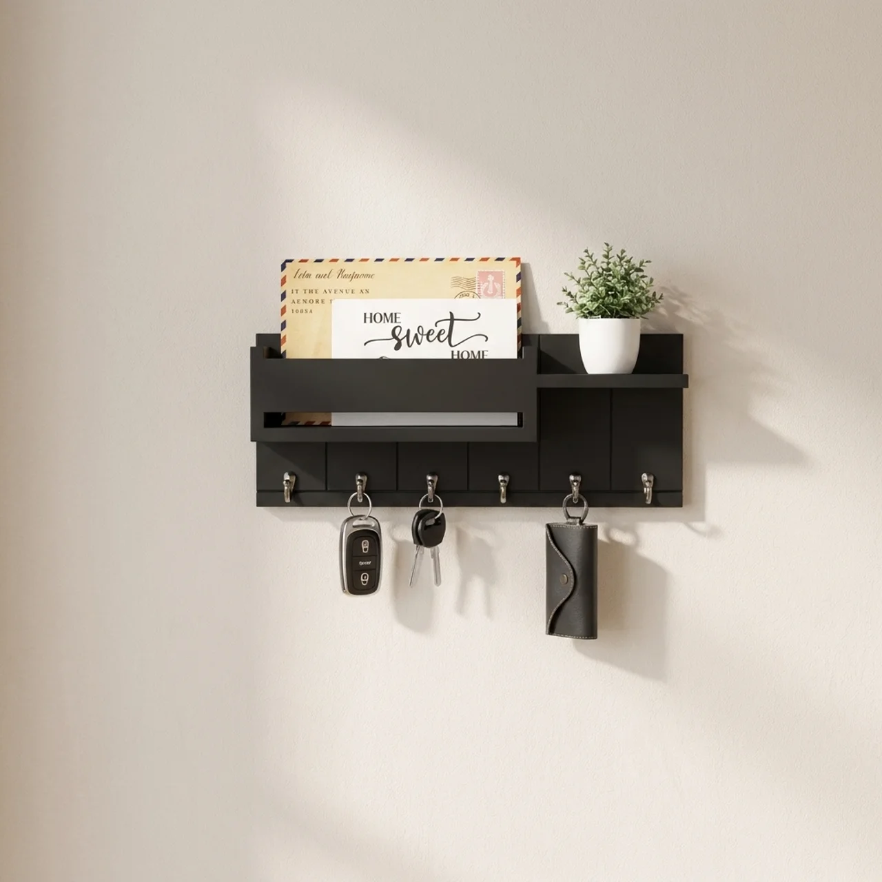Black wall-mounted shelf with key hooks and a small plant on a beige wall.