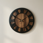 Wooden wall clock with black frame and Roman numerals on a beige wall.