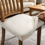 Person adjusting a textured white chair cover on a wooden chair in a living room setting.