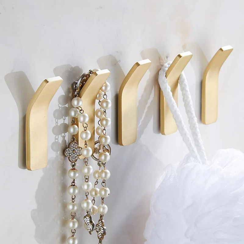 Gold wall hooks holding a pearl necklace and white fabric on a light gray background