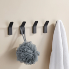 Four black hooks on a beige wall with a loofah and towel hanging from them.
