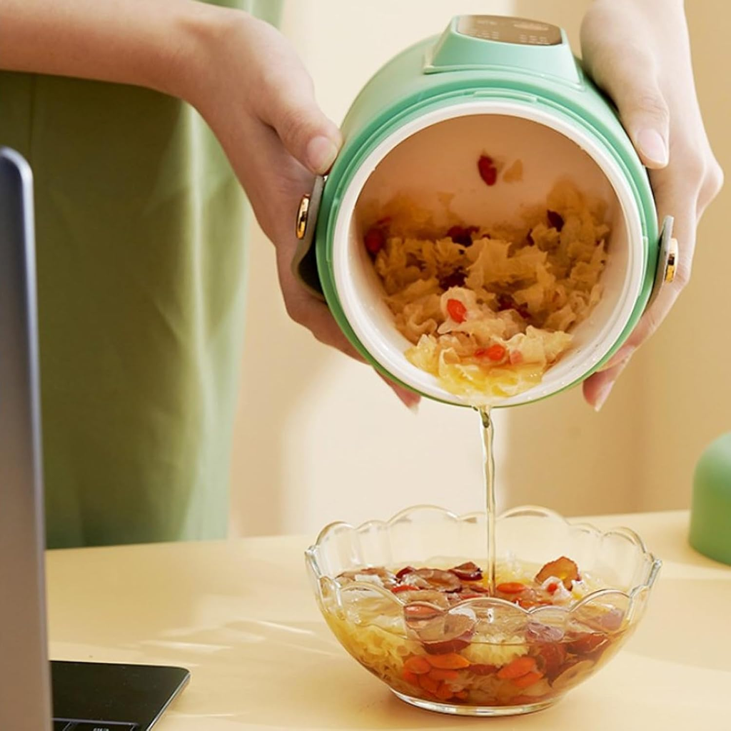 Person pouring food from a thermos into a glass bowl on a desk.