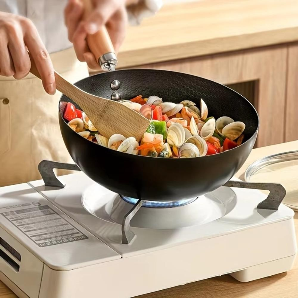 Person cooking clams and vegetables in a black wok on a portable stove.