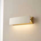 Modern wall light fixture with gold frame and white glass on a neutral wall.
