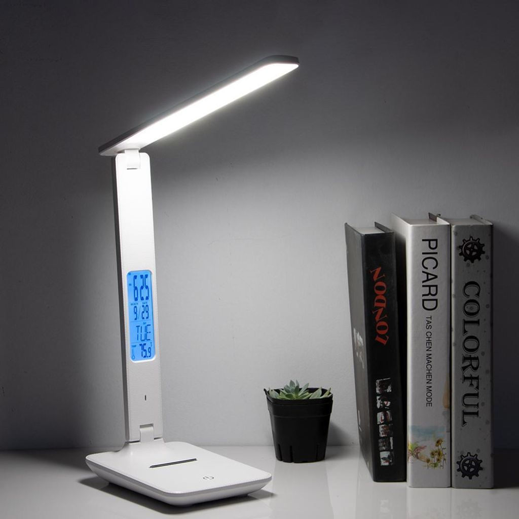 Table lamp with digital display on a desk next to books and a small plant.