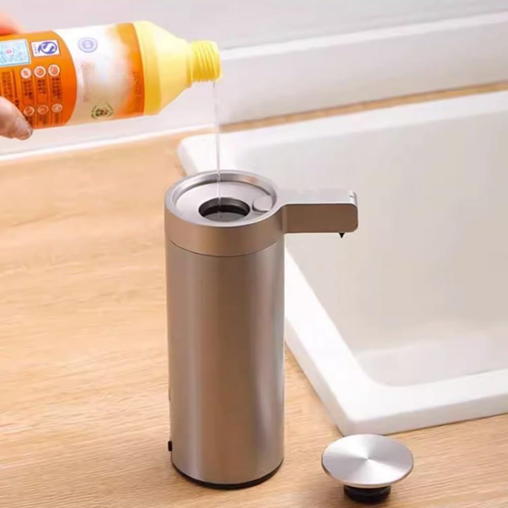 Hand pouring liquid soap into a metallic dispenser on a wooden surface with a sink in the background.