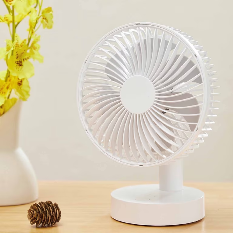 White desk fan on a wooden surface with yellow flowers and a pine cone in the background