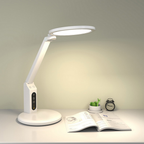 White LED desk lamp on a table with an open book and small plant