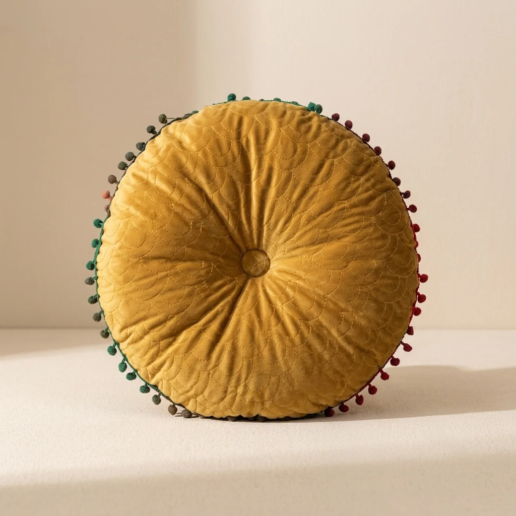 Round mustard yellow pillow with decorative pom-pom trim on a beige background