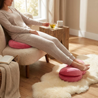 Person sitting on a chair with a pink foot rest, reading a book, and sipping tea.
