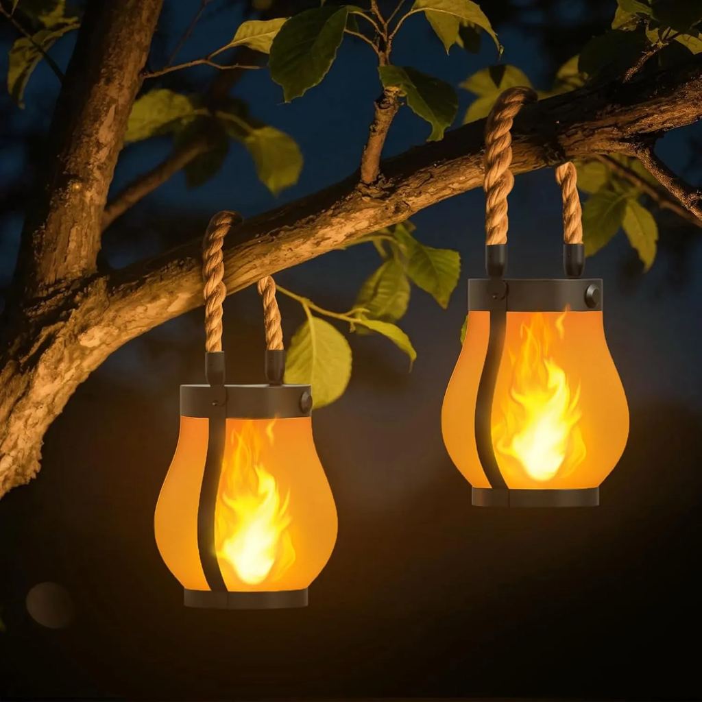 Two flame-shaped lanterns hanging from a tree branch at night.