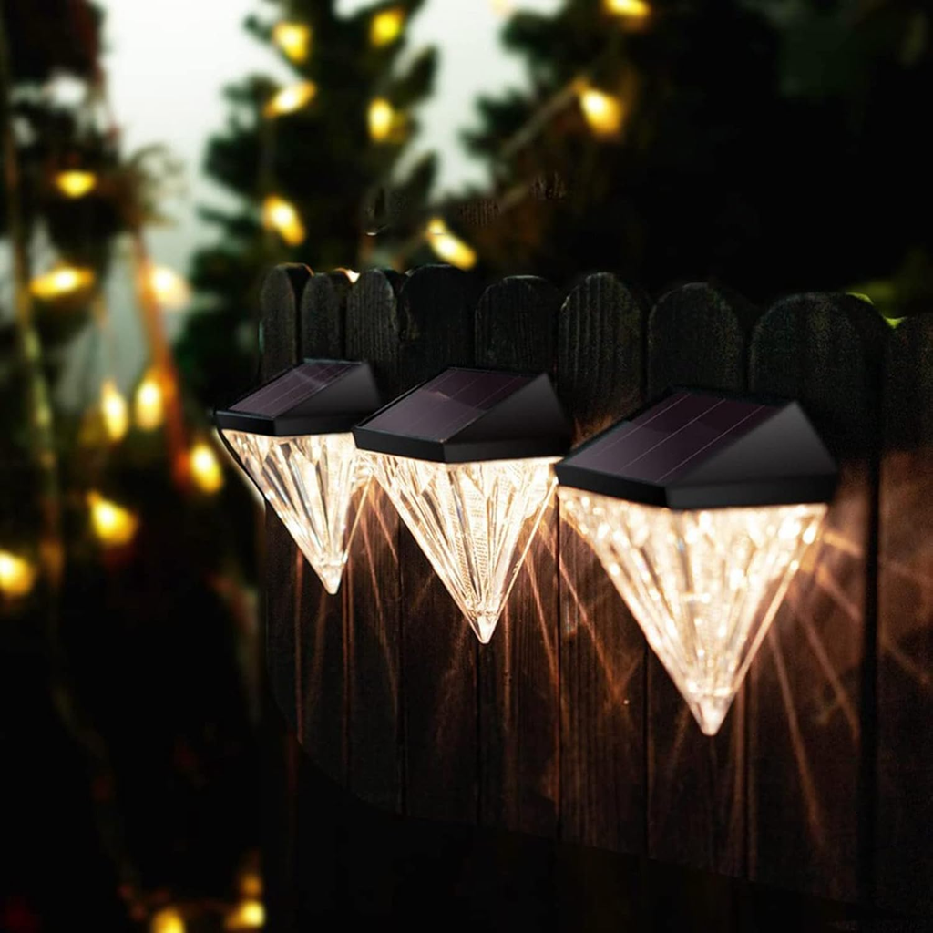Three diamond-shaped solar lights on a wooden fence with blurred lights in the background