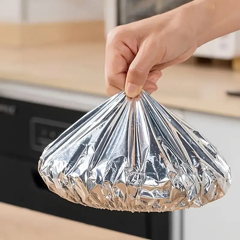 Hand holding a shiny silver bag against a blurred kitchen background