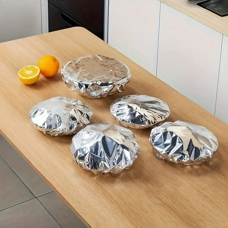 Silver foil-wrapped dishes on a kitchen counter with oranges.
