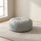 Round gray ottoman in a room with a window and beige walls.