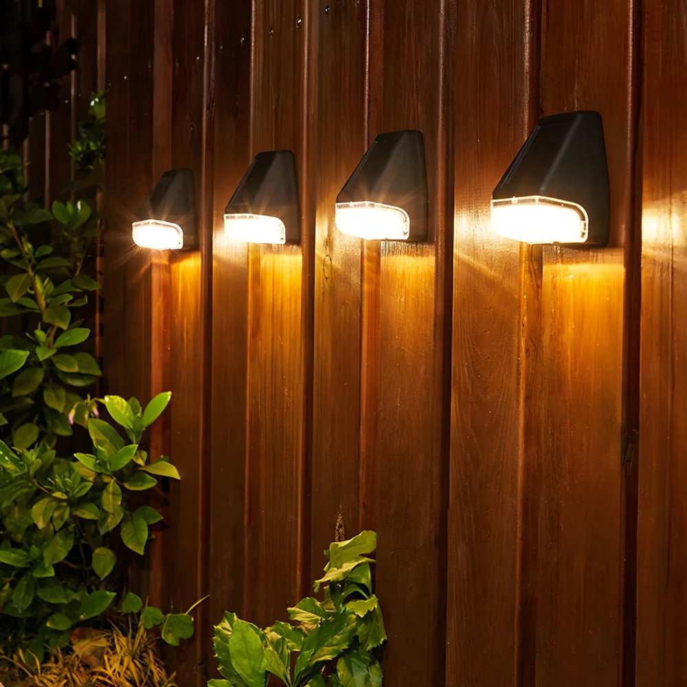 Four outdoor wall lights mounted on a wooden fence with plants in the foreground.