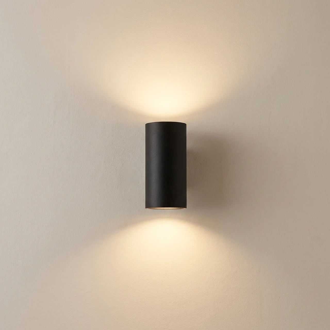 Black cylindrical wall light fixture on a beige wall