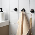 Black hooks on a tiled bathroom wall with beige towels hanging from them.