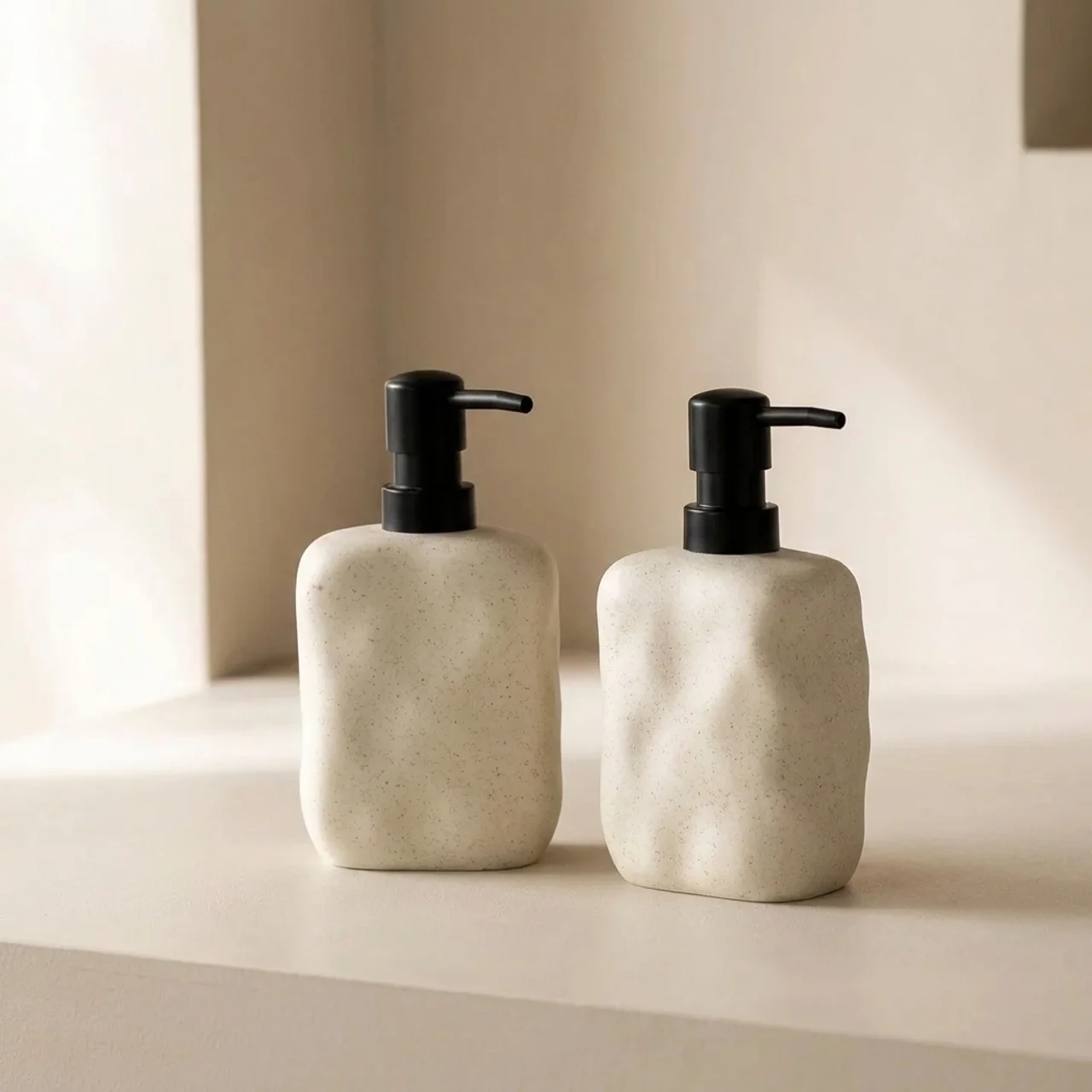 Two beige soap dispensers with black pumps on a neutral background