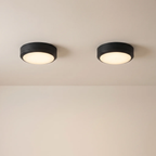 Two modern flush-mount ceiling lights with matte black circular frames and warm white glowing diffusers, installed side-by-side on a beige ceiling.