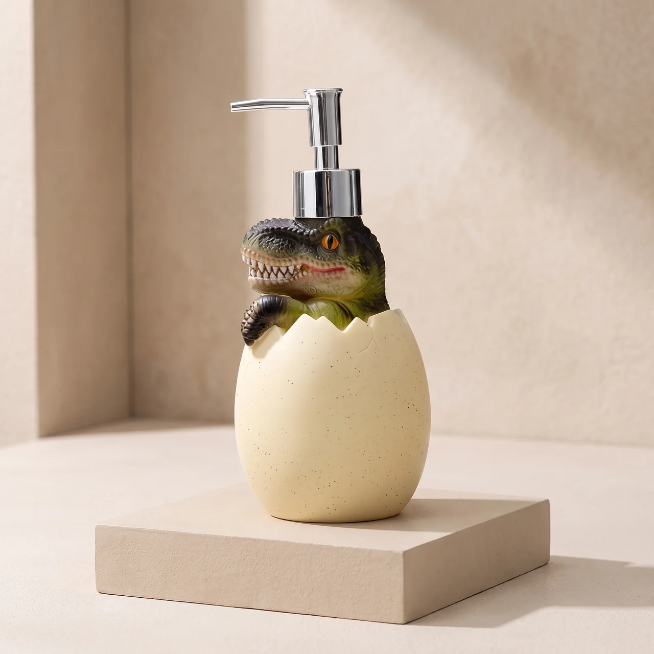 A dinosaur-themed soap dispenser featuring a realistic green and black dinosaur peeking out of a speckled cream-colored egg-shaped base, with a chrome pump. The dispenser is displayed on a matching beige pedestal against a neutral beige background.