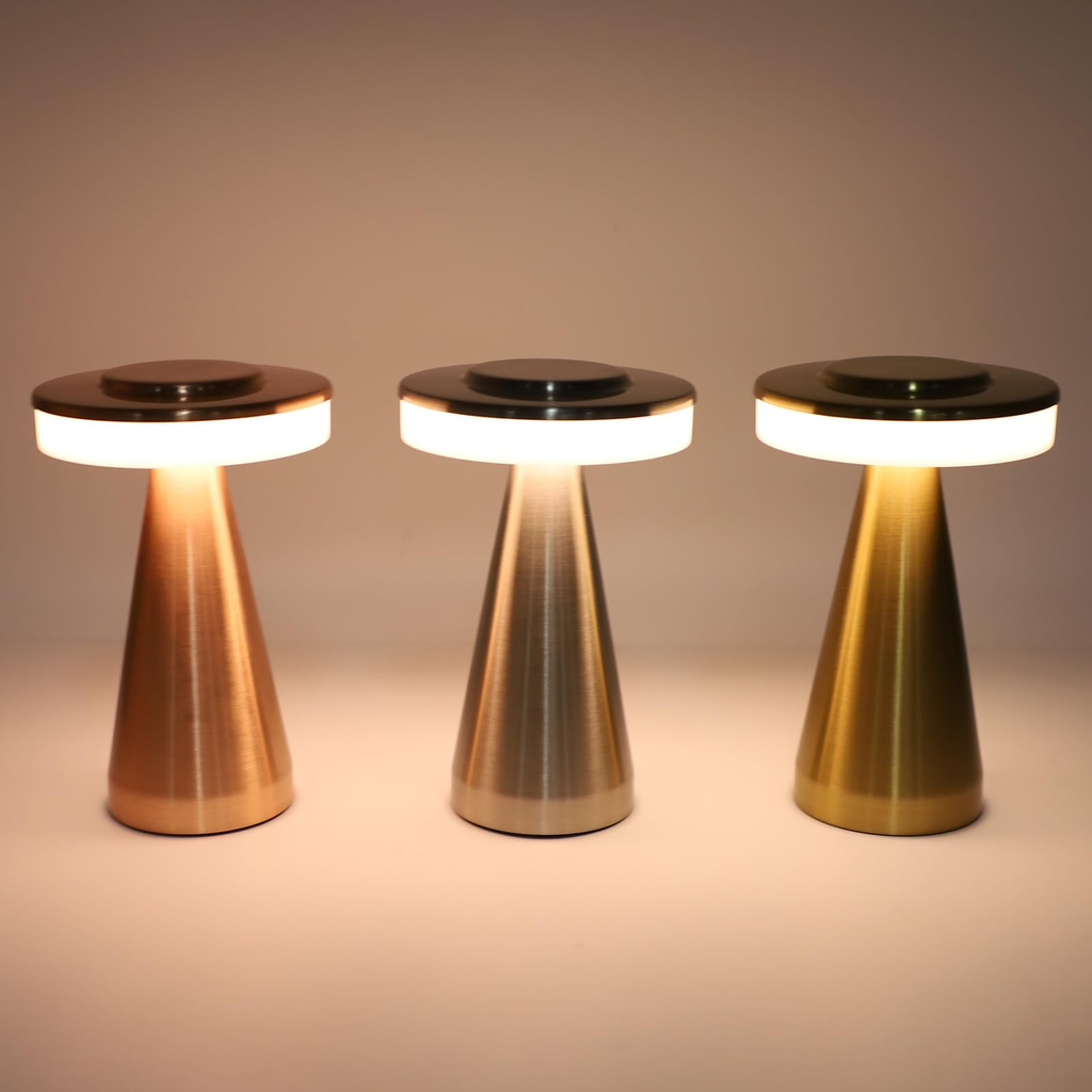 Three modern table lamps with brushed metal cone-shaped bases and glowing white circular light bands, shown in copper, silver, and gold finishes against a warm beige background.