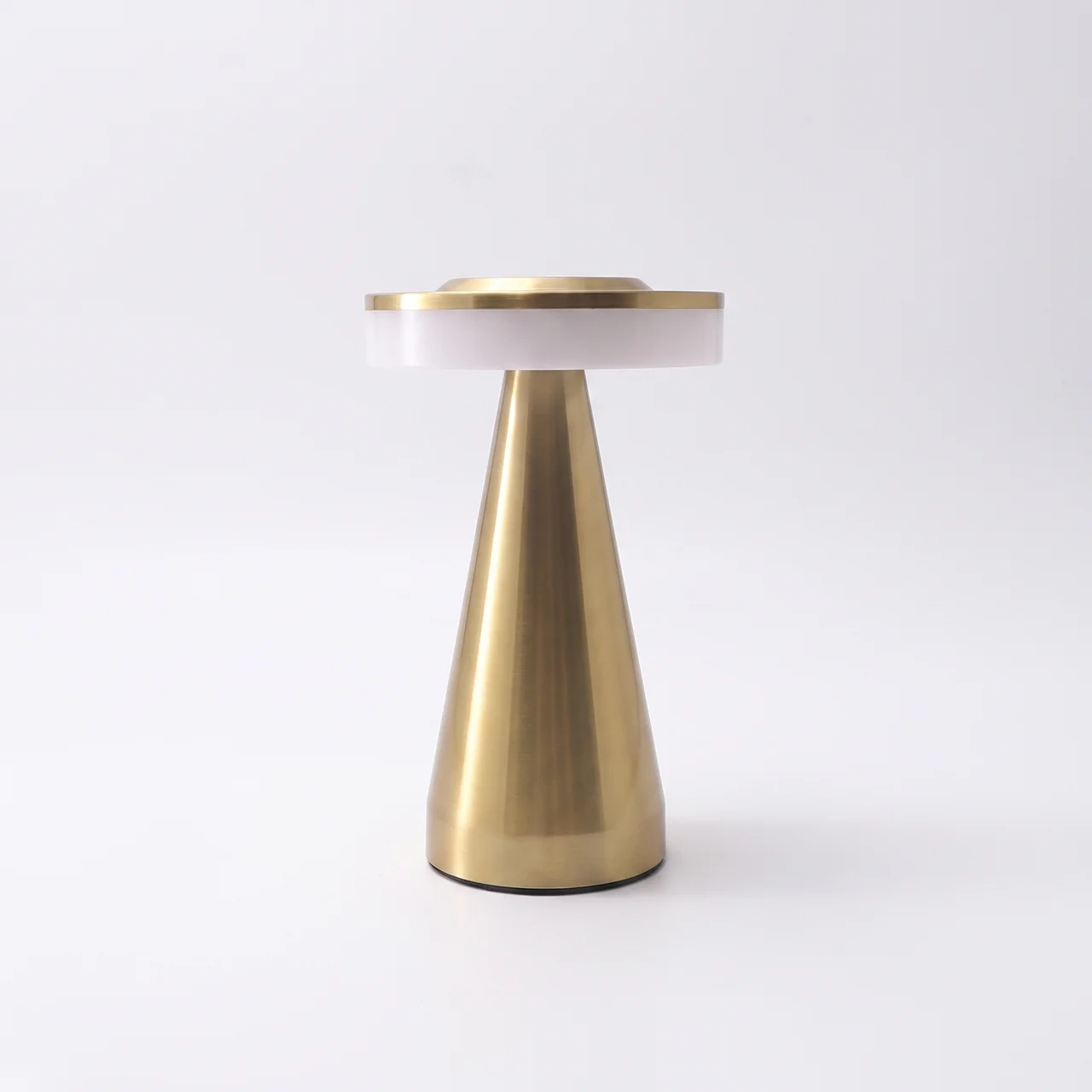 A modern table lamp with a tapered brushed brass base, a white cylindrical shade, and a brushed brass top rim, photographed on a seamless white background.