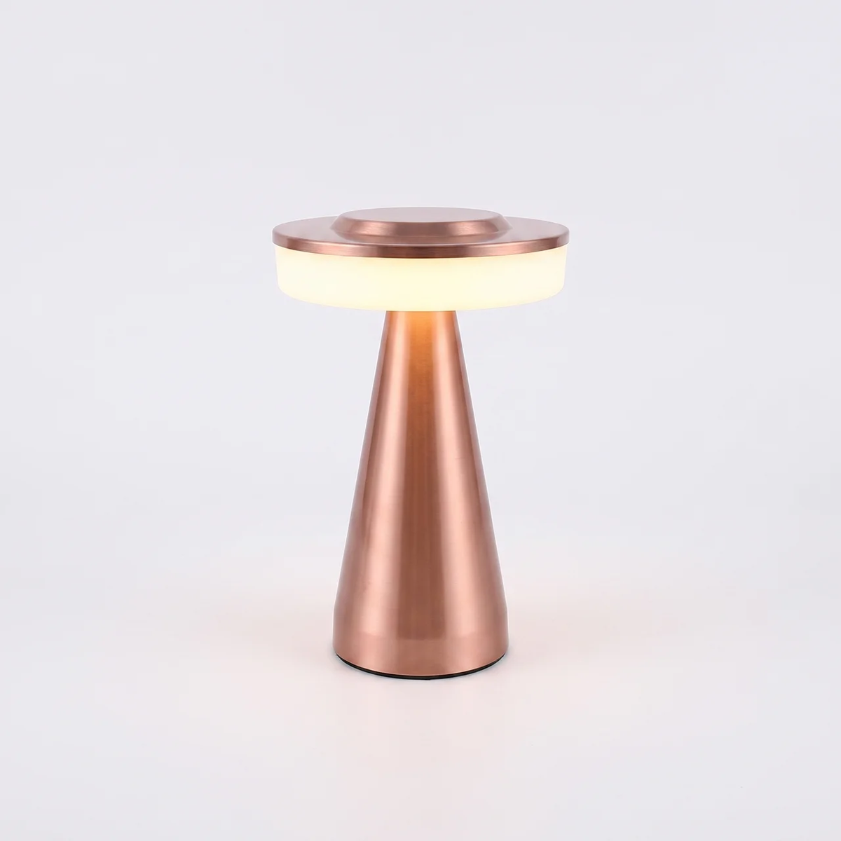 A modern table lamp with a tapered metallic rose gold base and a circular glowing white diffuser on top, set against a clean white background.