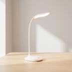 A modern white flexible gooseneck desk lamp with a glowing illuminated light bar, resting on a light wood table against a neutral beige wall.