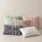 Five fluffy faux-fur throw pillows in soft pastel and neutral tones, including mint green, blush pink, taupe, gray, and white, arranged against a warm beige background.