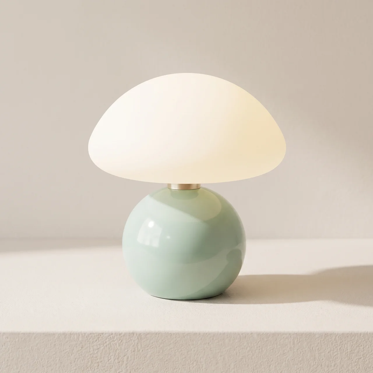 A mushroom-shaped table lamp with a glossy pale green spherical base and a frosted white dome shade, shown lit on a light beige surface against a neutral background.