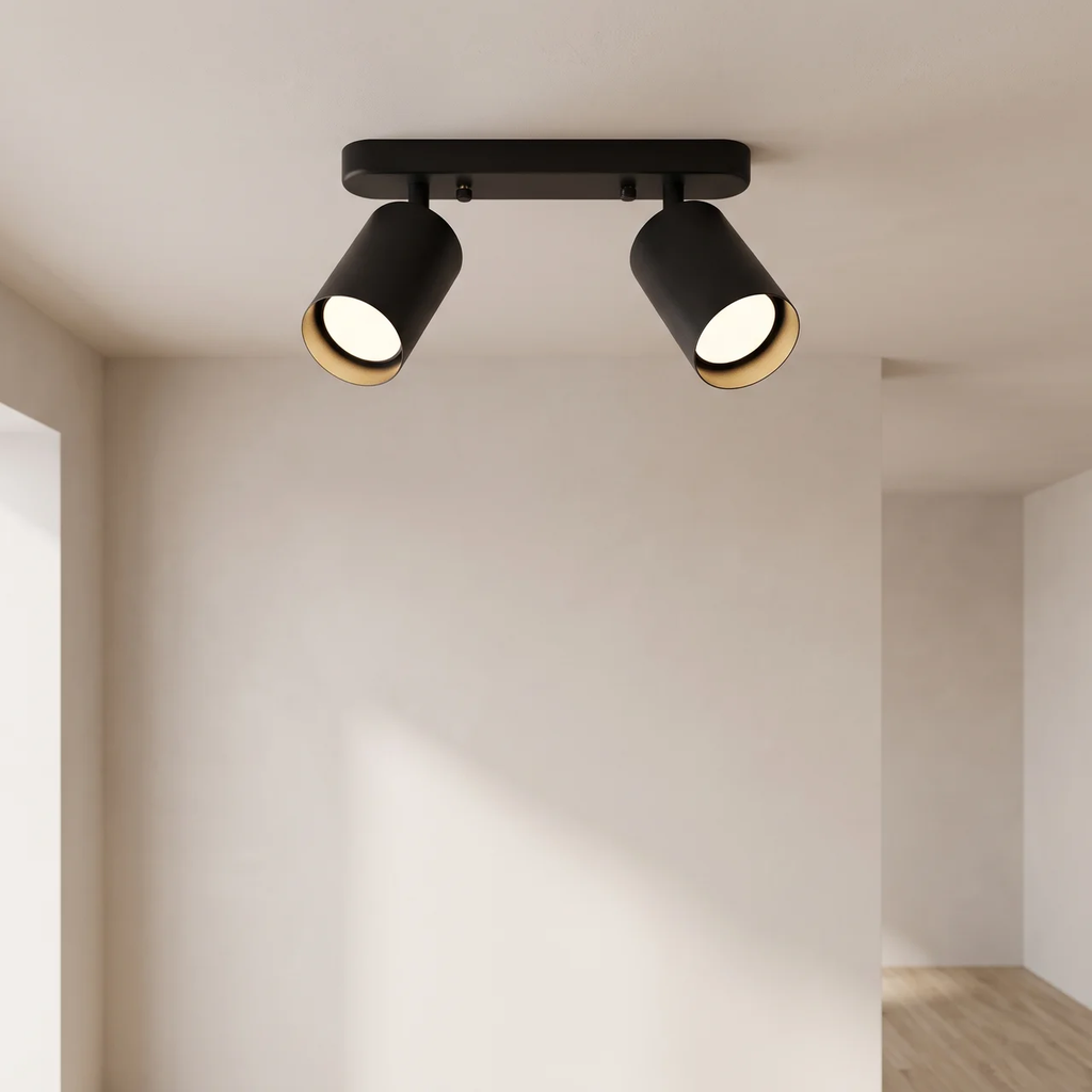 A modern two-light track ceiling fixture in matte black with warm gold-toned inner trim, mounted on a white ceiling in a minimalist room.