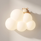 A warm white cloud-shaped wall sconce with a small sleeping deer figurine on top, mounted on a light beige wall with soft shadows.