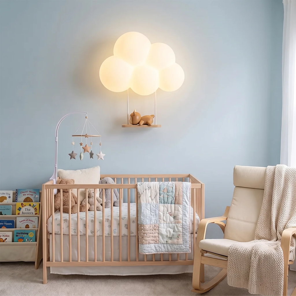 A glowing cloud-shaped wall lamp mounted above a wooden crib in a softly styled nursery with pale blue walls, a rocking chair, and a quilted blanket.