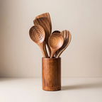 A set of wooden kitchen utensils, including a slotted spoon, spatula, and serving spoons, arranged in a cylindrical wooden holder against a neutral beige background.