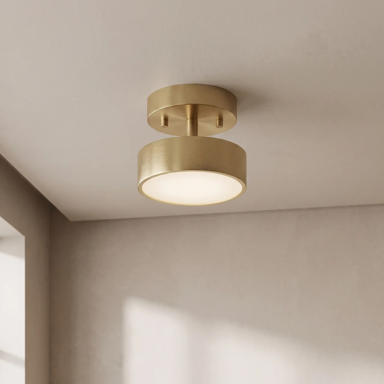 A modern semi-flush mount ceiling light fixture in a brushed gold finish, emitting a warm glow from its circular shade, shown installed on a textured off-white ceiling in a minimalist room corner.