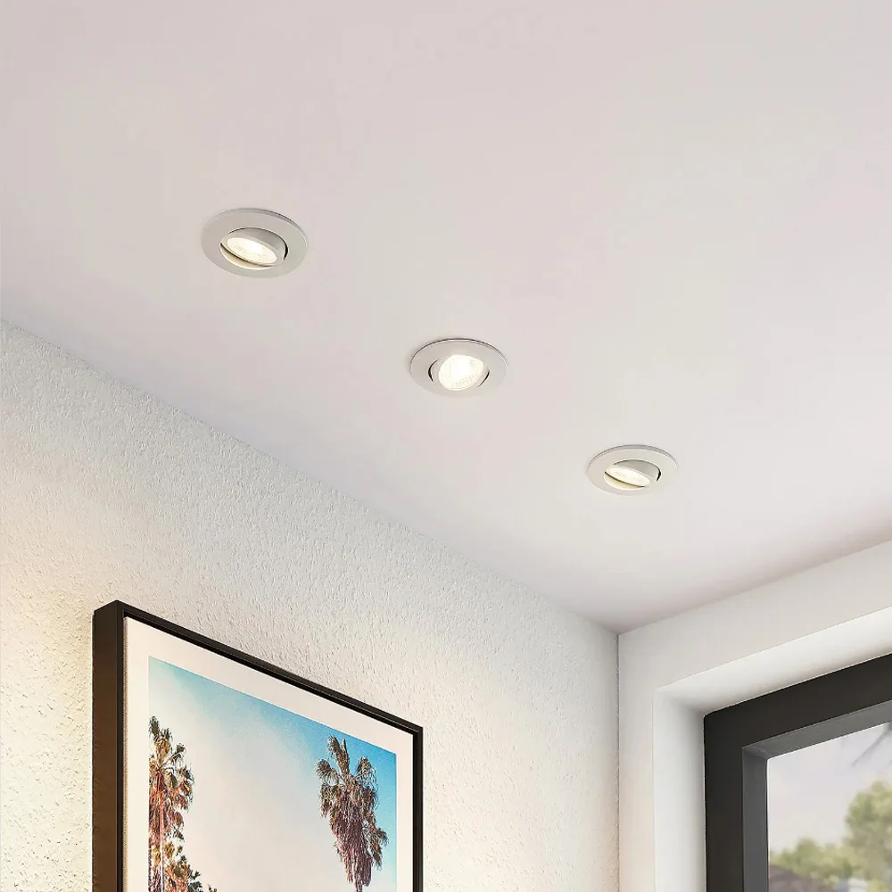 Three round recessed ceiling lights installed in a white textured ceiling, with a framed palm tree print on the wall below.