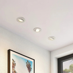 Three round recessed ceiling lights installed in a white textured ceiling, with a framed palm tree print on the wall below.
