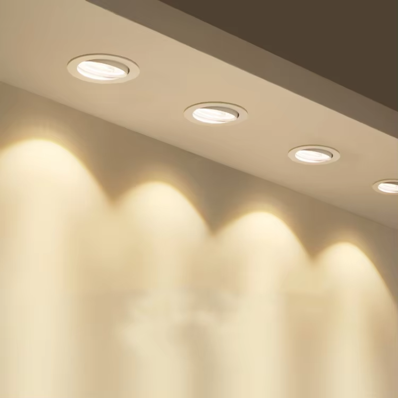 Four round recessed ceiling lights installed in a white ceiling, casting warm yellow light beams onto the wall below.