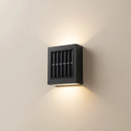 A modern square black outdoor wall sconce with a vented front and warm LED lighting, mounted on a beige wall.