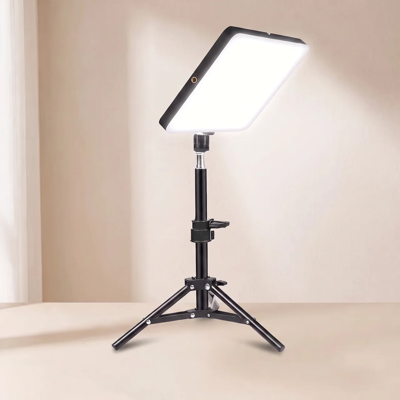 A rectangular LED light panel on a black adjustable tripod stand, photographed in a clean indoor studio setup with a warm beige wall and floor.